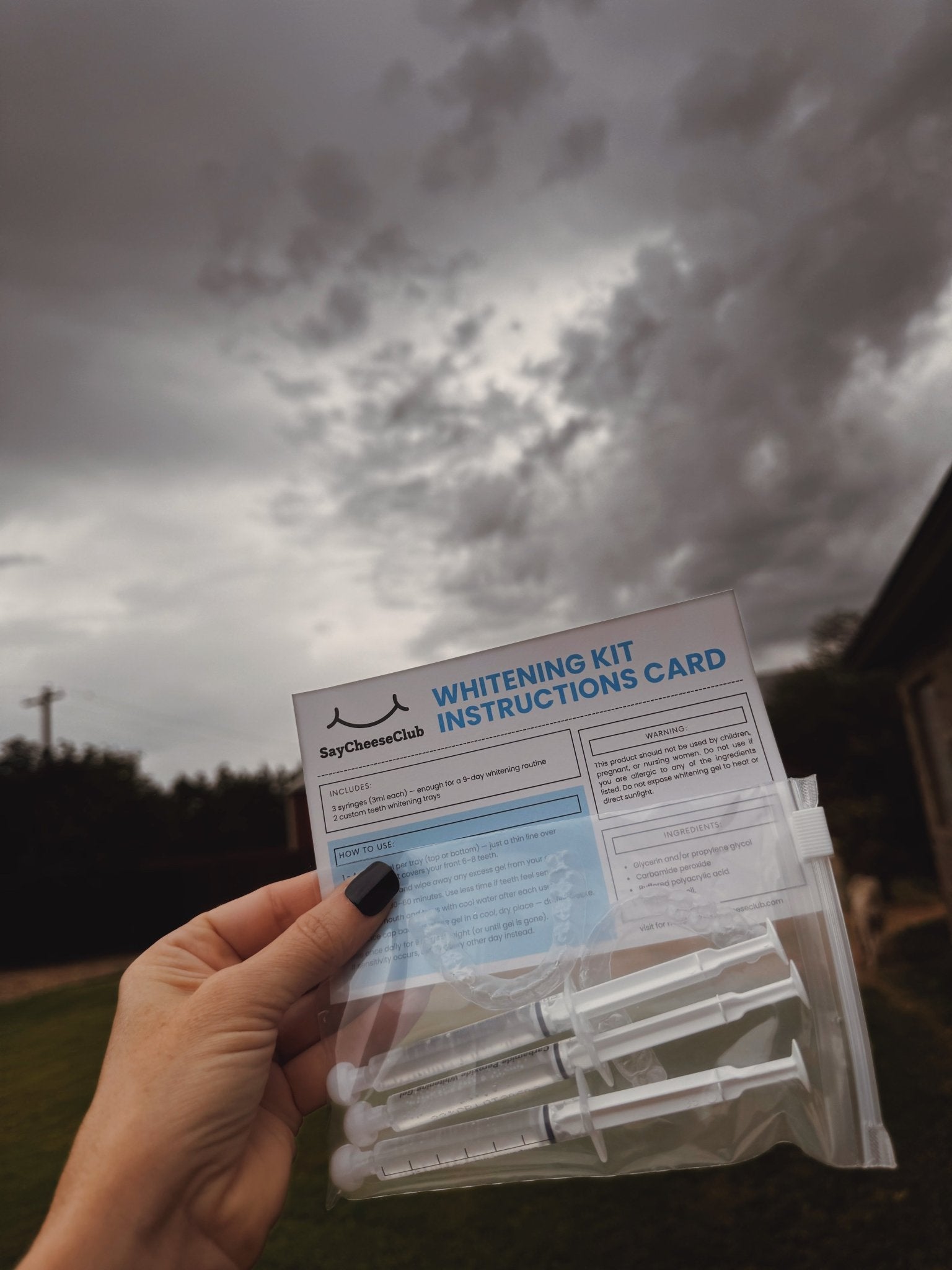 SayCheeseClub Teeth Whitening Kit Held in Air — clouds in background